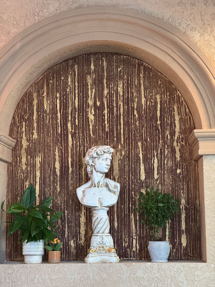 Elegant archway with classical bust surrounded by potted plants. Perfect for interior design inspiration.